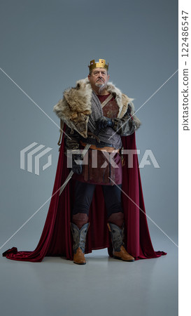 Portrait of serious elderly man, medieval king in golden crown, wearing amour, exuding royalty and leadership against grey studio background Portrait of serious elderly man, medieval king in golden crown, wearing amour, exuding royalty and leadership against grey studio background 122486547