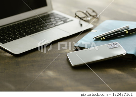 Image of business at home: laptop computer on desk, smartphone, notebook and pen, glasses Image of business at home: laptop computer on desk, smartphone, notebook and pen, glasses 122487161