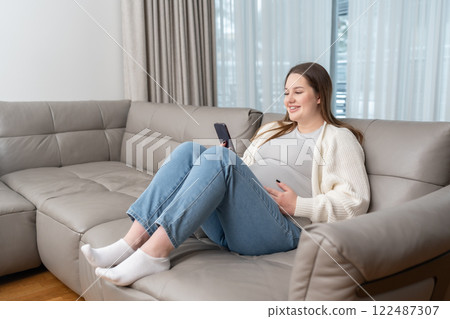 Smiling pregnant woman sitting on sofa at home using smartphone for online shopping and digital services with copy space. Concept of maternity, digital connection, technology and ecommerce convenience Smiling pregnant woman sitting on sofa at home using smartphone for online shopping and digital services with copy space. Concept of maternity, digital connection, technology and ecommerce convenience 122487307