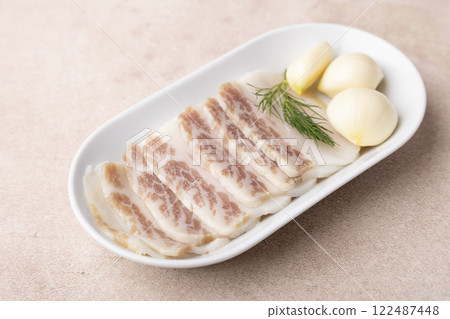 Homemade salted pork lard, sliced, with garlic cloves on a white plate. Traditional Russian and Ukrainian appetizer for vodka, borsch, shchi, soup. Homemade dish made from subcutaneous pig fat. 122487448