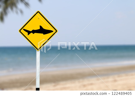 A bright yellow warning sign with a shark symbol, alerting beachgoers to avoid swimming in the area due to potential shark danger, ensuring public safety. A bright yellow warning sign with a shark symbol, alerting beachgoers to avoid swimming in the area due to potential shark danger, ensuring public safety. 122489405
