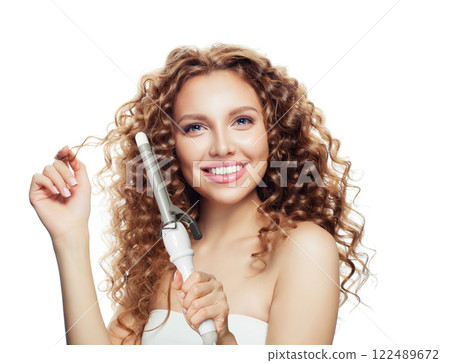 Excited woman with curly hairstyle using hot curling tongs iron, indoor fashion portrait.  122489672