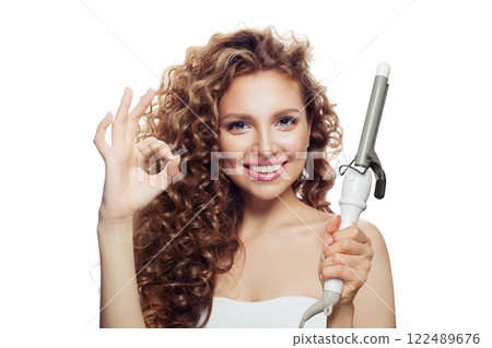 Positive woman with curly hairstyle using hot curling tongs iron, indoor fashion portrait.  122489676