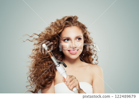 Charming woman with curly hairstyle using hot curling tongs iron, indoor fashion portrait. Charming woman with curly hairstyle using hot curling tongs iron, indoor fashion portrait. 122489679