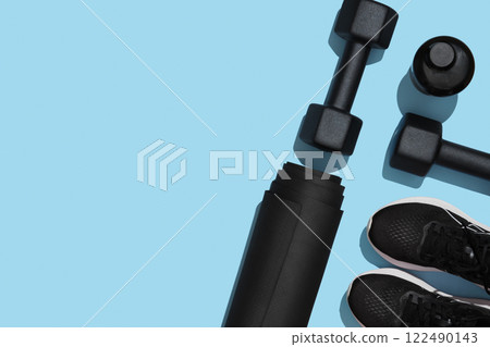 Black workout equipment, dumbbells, mat, sneakers and water bottle on blue background. Fitness, sports items, healthy lifestyle concept. Space for your text 122490143