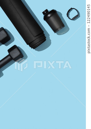 Vertical fitness banner with black dumbbells, mat, water bottle and fitness band on blue background. Fitness, sports items, healthy lifestyle concept. Space for your text 122490145