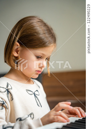 Home lesson on music for the girl on white piano synthesizer. Concept of early development: learning music enhances motor skills, hearing, and intelligence, fostering creativity from childhood Home lesson on music for the girl on white piano synthesizer. Concept of early development: learning music enhances motor skills, hearing, and intelligence, fostering creativity from childhood 122490229
