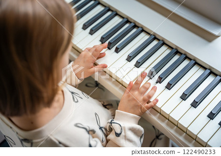 Home lesson on music for the girl on white piano synthesizer. Concept of early development: learning music enhances motor skills, hearing, and intelligence, fostering creativity from childhood Home lesson on music for the girl on white piano synthesizer. Concept of early development: learning music enhances motor skills, hearing, and intelligence, fostering creativity from childhood 122490233