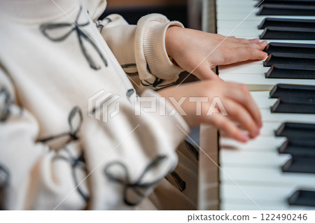 Close up view of small hands of girl on white piano synthesizer. Concept of early development: learning music enhances motor skills, hearing, and intelligence, fostering creativity from childhood Close up view of small hands of girl on white piano synthesizer. Concept of early development: learning music enhances motor skills, hearing, and intelligence, fostering creativity from childhood 122490246