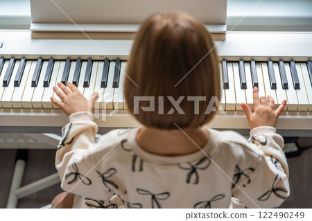 Home lesson on music for the girl on white piano synthesizer. Concept of early development: learning music enhances motor skills, hearing, and intelligence, fostering creativity from childhood Home lesson on music for the girl on white piano synthesizer. Concept of early development: learning music enhances motor skills, hearing, and intelligence, fostering creativity from childhood 122490249