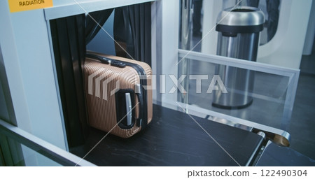 Security Checkpoint in Airport Terminal: Passenger Places Suitcase on Conveyor Belt for Baggage Screening 122490304