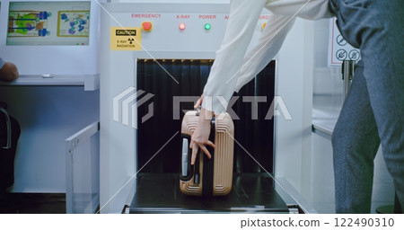 Airport Security Checkpoint: Passenger Places Suitcase on Conveyor Belt for X-ray Luggage Scanning Airport Security Checkpoint: Passenger Places Suitcase on Conveyor Belt for X-ray Luggage Scanning 122490310