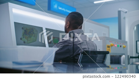 Security Officer Monitors Baggage Screening on Computer Screens. Passengers Putting Personal Items in Trays Security Officer Monitors Baggage Screening on Computer Screens. Passengers Putting Personal Items in Trays 122490340