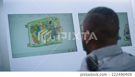 Back View of Security Officer Monitoring Baggage X-ray Scanning on Computer Screens 122490409