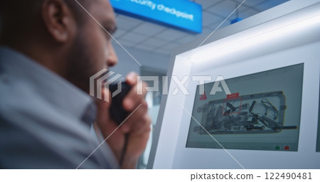 Airport Terminal: Security Officer Monitors X-ray Luggage Scanning on Screens, Finds Suspicious Item 122490481