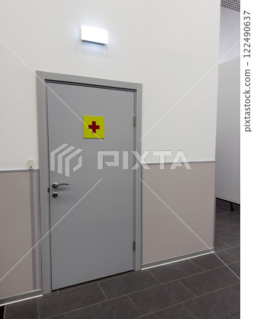 Hospital interior with entrance door and first aid sign, door to doctor office in corridor of medical building. Medical aid point for people, vertical photo Hospital interior with entrance door and first aid sign, door to doctor office in corridor of medical building. Medical aid point for people, vertical photo 122490637