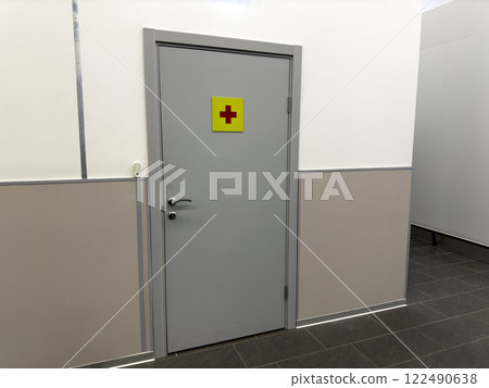Hospital corridor with gray door and sign with red cross. Entrance door to medical facility for helping people. First aid station, interior of modern medical center 122490638