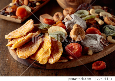 Dried mango slices, tropical fruits, nuts, and raisins on a wooden table. Dried mango slices, tropical fruits, nuts, and raisins on a wooden table. 122491184