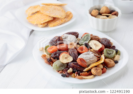 Mix of dried tropical fruits, nuts, and raisins on a white table. 122491190