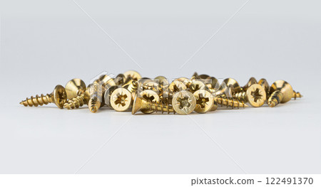 A pile of golden screws lies on a white surface ready for various projects 122491370