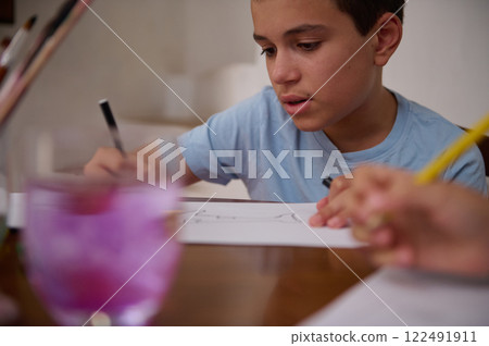 Focused young boy engaged in drawing and writing at a wooden table 122491911