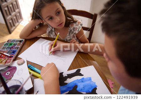 Two children drawing with watercolors and pencils at a wooden table Two children drawing with watercolors and pencils at a wooden table 122491939