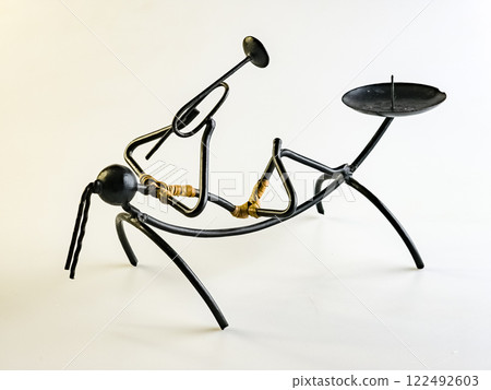 Candlestick made of black wire in the shape of a woman playing a trumpet on a white background Candlestick made of black wire in the shape of a woman playing a trumpet on a white background 122492603