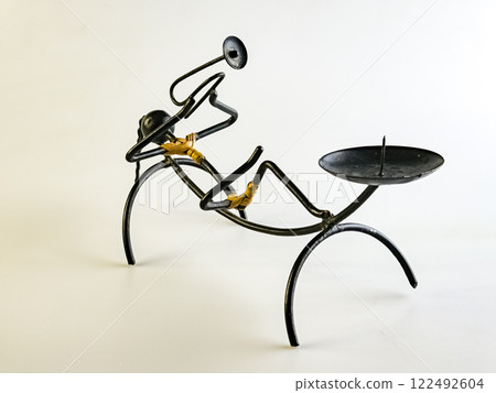 A candlestick made of black wire in shape of a woman playing a trumpet on a white background A candlestick made of black wire in shape of a woman playing a trumpet on a white background 122492604