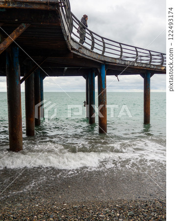 Metal pier on columns. Construction on the sea.Rusty pier. Resort place in winter on a cloudy day. 122493174