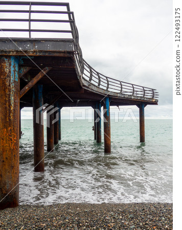 Metal pier on columns. Construction on the sea. Resort place in winter on a cloudy day. Metal pier on columns. Construction on the sea. Resort place in winter on a cloudy day. 122493175