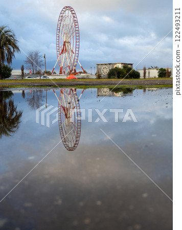 Reflection of a ferris wheel in a puddle. Resort town after the rain. Batumi ferris wheel. 122493211