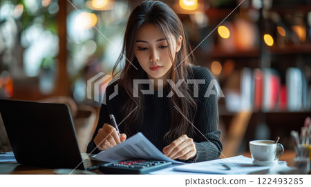 Focused woman analyzing documents and data with laptop in cozy cafe environment Focused woman analyzing documents and data with laptop in cozy cafe environment 122493285