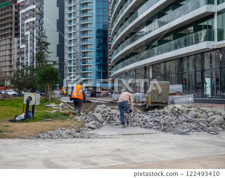 Workers break off concrete. Hard work. People are reconstructing the sidewalk. Bricklayers. 122493410
