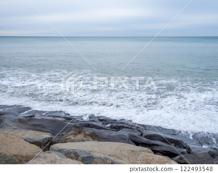rocky shore is washed by the waves in cloudy weather. Black Sea coast. The coast of Batumi. Nature in shades of grey.  boring landscape 122493548