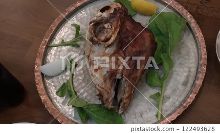 Roasted Lamb Head with Fresh Greens and Lemon on a Decorative Metal Plate Roasted Lamb Head with Fresh Greens and Lemon on a Decorative Metal Plate 122493628