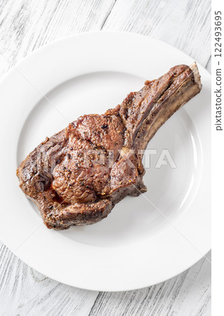 Whole Grilled Medium-Rare Cowboy Steak on White Plate, Wooden Table 122493695
