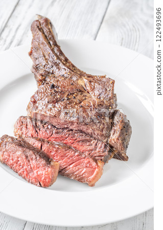 Sliced Grilled Medium-Rare Cowboy Steak on White Plate and Table 122493696