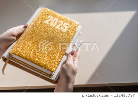 Gold colored diary, pen on bright background. New year planning concept. Minimalistic workstation. 122493757