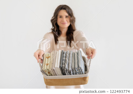 Beautiful European woman in beige suit holds wicker stylish basket with neatly folded pillowcases Beautiful European woman in beige suit holds wicker stylish basket with neatly folded pillowcases 122493774