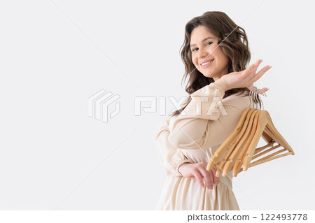 Beautiful European woman in beige dress holding several empty wooden clothes hangers Beautiful European woman in beige dress holding several empty wooden clothes hangers 122493778