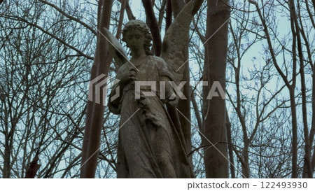 A beautiful Serene Stone Angel Statue nestled amidst lush, vibrant greenery, exuding peace and A beautiful Serene Stone Angel Statue nestled amidst lush, vibrant greenery, exuding peace and 122493930