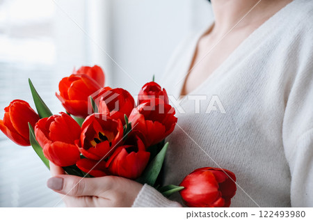 Close-up of a woman in a white sweater with a bouquet of red tulips Close-up of a woman in a white sweater with a bouquet of red tulips 122493980
