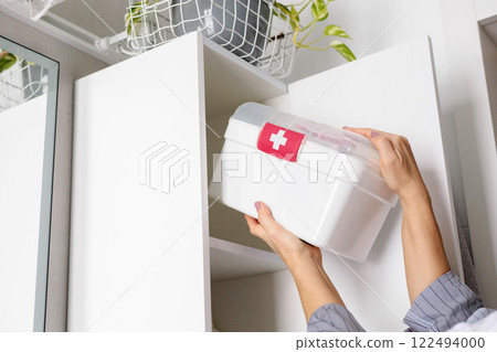 Female hands putting first aid kit with vitamins, drugs, antibiotics and cure at bathroom cupboard. Female hands putting first aid kit with vitamins, drugs, antibiotics and cure at bathroom cupboard. 122494000