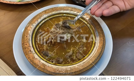 A Hand Serving a Spoonful of Traditional Turkish Kelle Paca Soup from Ornate Bowl 122494071