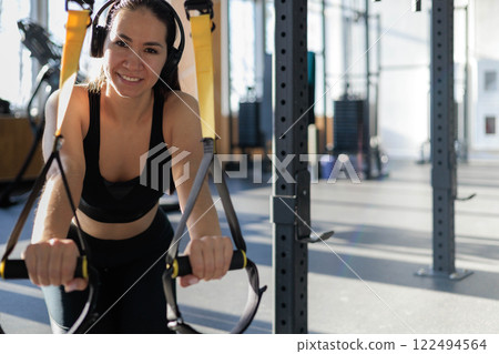 Young beautiful Asian woman doing fitness exercises with TRX exercise bands in gym. 122494564