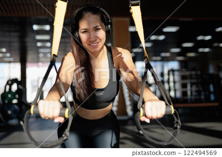 Young beautiful Asian woman doing fitness exercises with TRX exercise bands in gym. Young beautiful Asian woman doing fitness exercises with TRX exercise bands in gym. 122494569