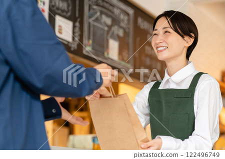 Middle-aged female cafe clerk handing over takeaway items 122496749