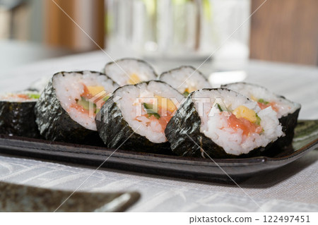 Homemade salmon salad sushi on black plate with white placemat on table. Japanese healthy food. Selective focus. Homemade salmon salad sushi on black plate with white placemat on table. Japanese healthy food. Selective focus. 122497451