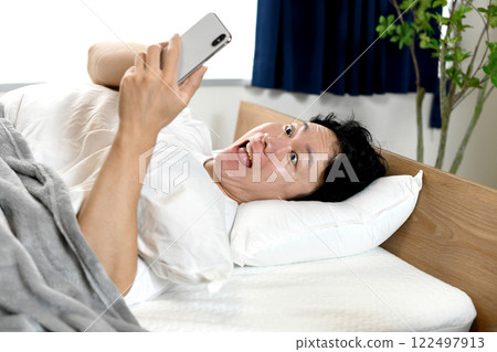 Surprised Asian man holding smartphone on bed 122497913