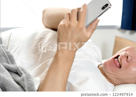 Surprised Asian man holding smartphone on bed 122497914